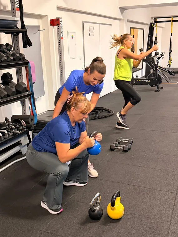 Trénerka vedie klientku pri cvičení s kettlebellom